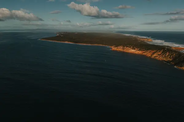 Un cap boisé et une mer sombre vus du ciel